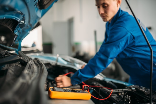 Car electrician performing a multimeter battery inspection