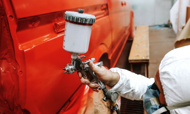 Worker with spray gun applying red paint